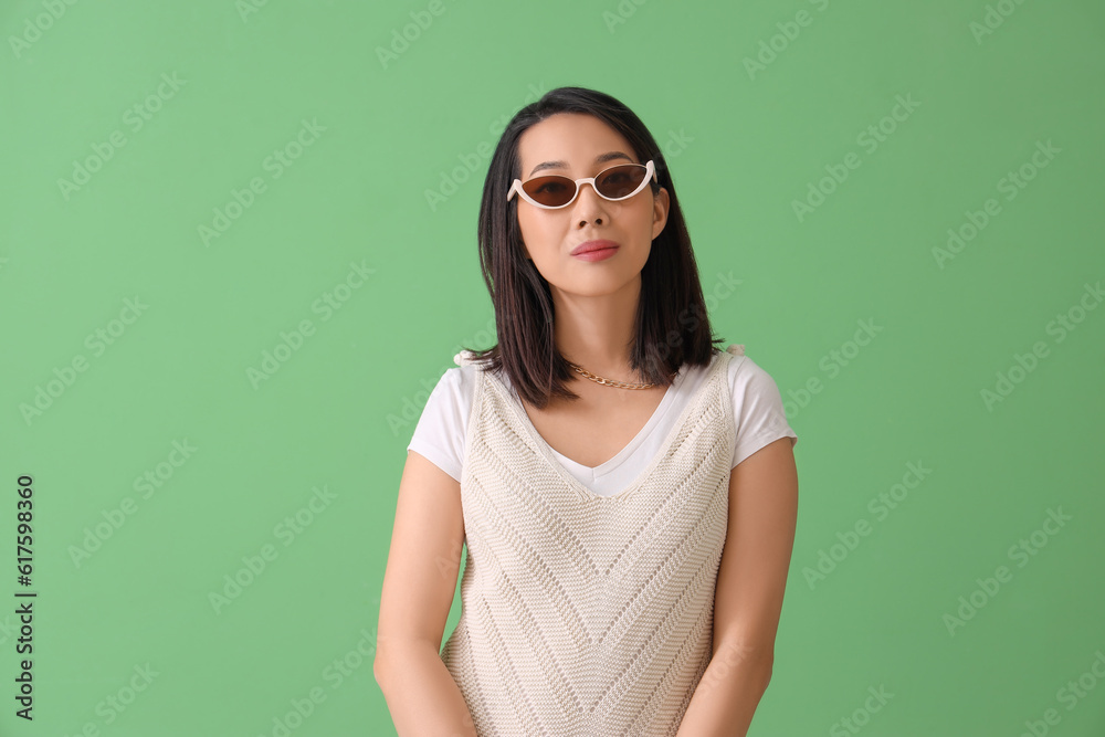 Beautiful Asian woman in stylish sunglasses on green background