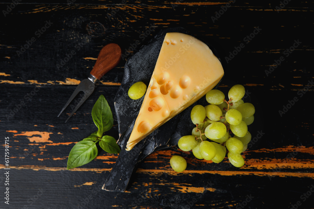 Board with tasty Swiss cheese on dark wooden background