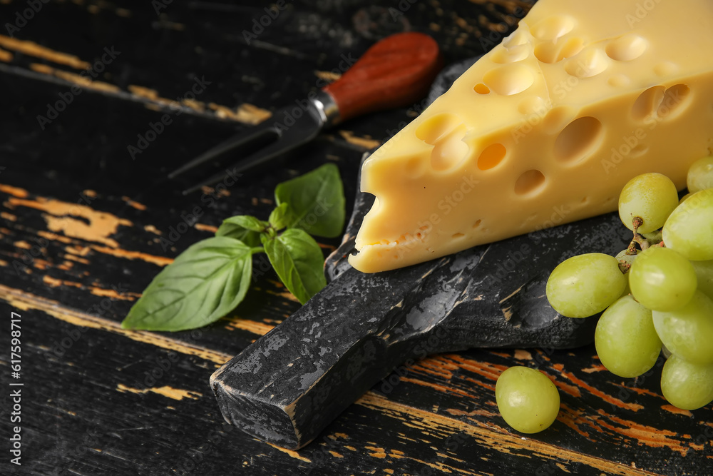 Board with tasty Swiss cheese on dark wooden background