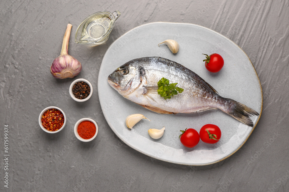 Plate of raw dorado fish with tomatoes and spices on grey background