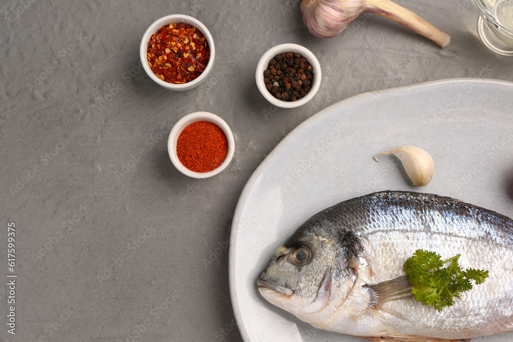 Plate of raw dorado fish with spices on grey background