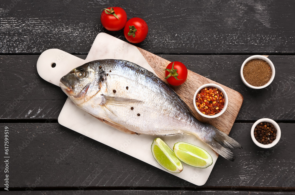 Board of raw dorado fish with lime, tomatoes and spices on dark wooden background