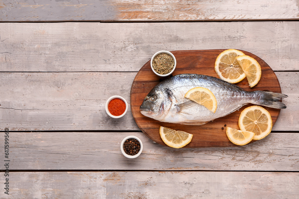 Board of raw dorado fish with lemon and spices on grey wooden background