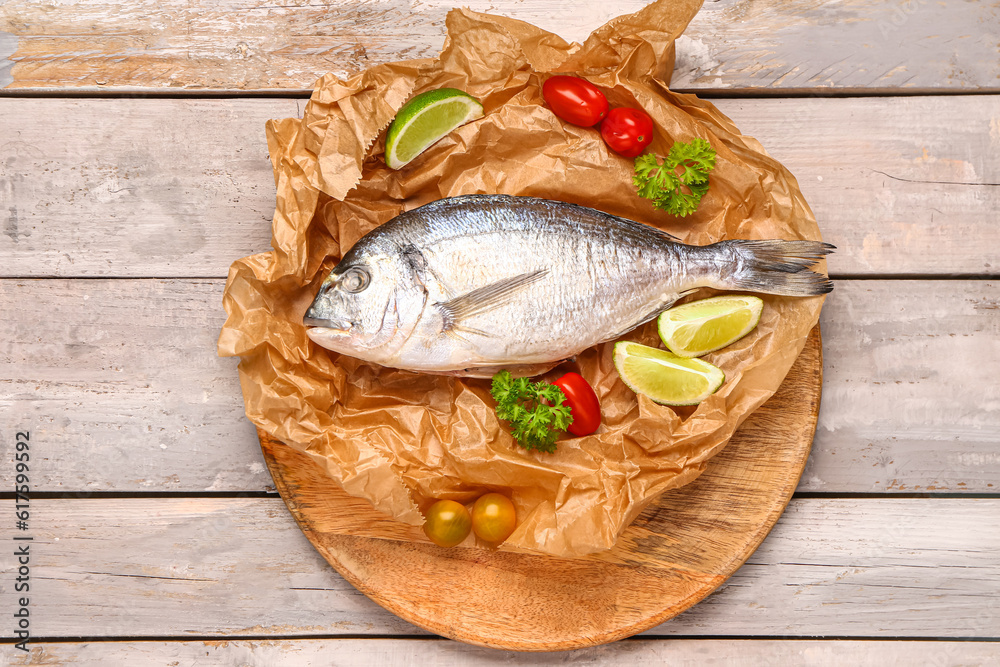 Board of raw dorado fish with lime and tomatoes on grey wooden background