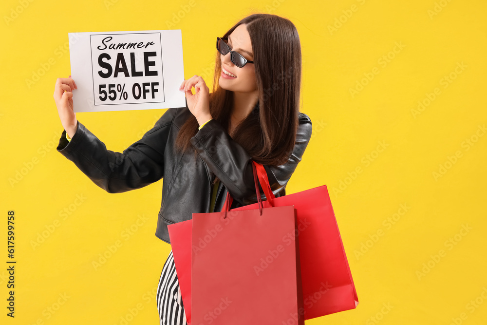 Young woman holding paper with text SUMMER SALE and shopping bags on yellow background