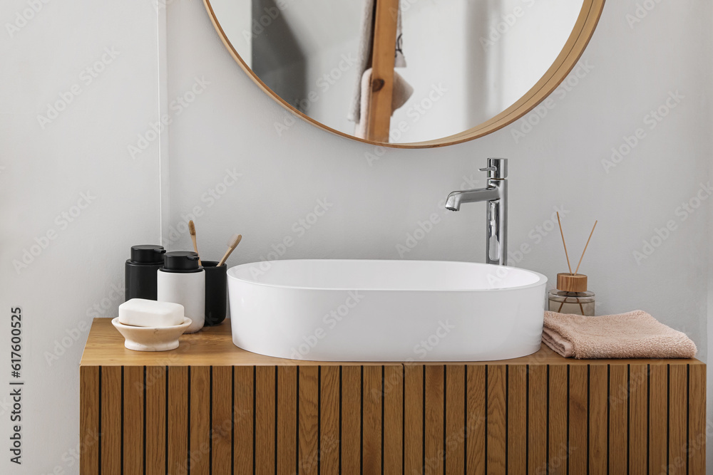 Sink bowl, soap bar, toothbrushes and bath accessories on wooden cabinet in bathroom