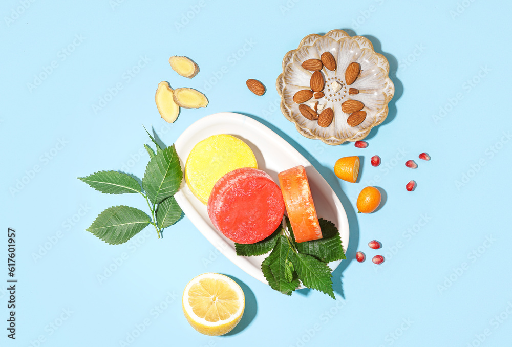 Plate with colorful solid shampoo bars, lemon and leaves on blue background