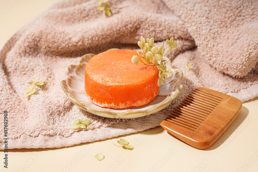 Plate with orange solid shampoo bar, dry lilac and comb on beige background