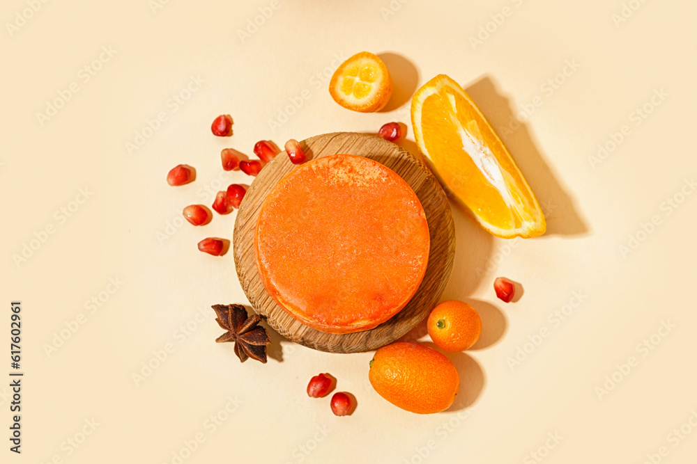 Wooden stand with solid shampoo bar with orange, kumquat and pomegranate on beige background