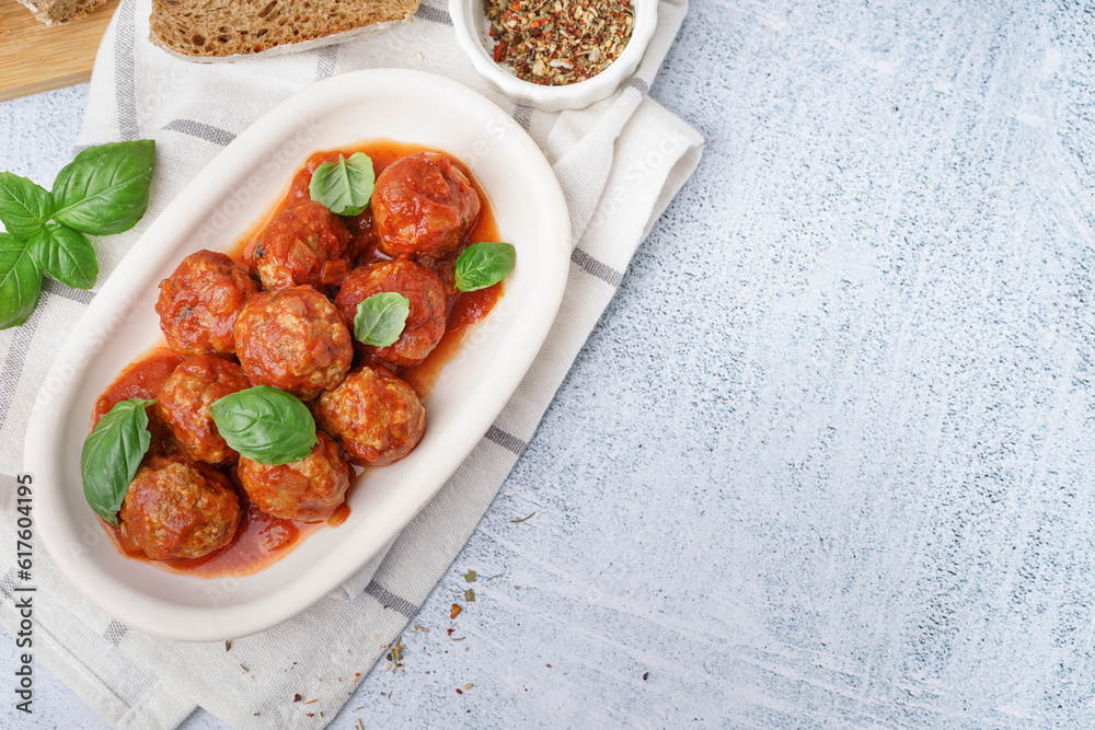 Plate of tasty meat balls with tomato sauce and basil on grey table