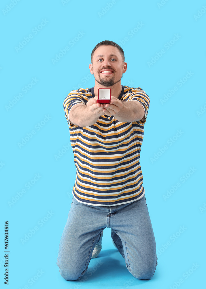 Handsome man with engagement ring on blue background