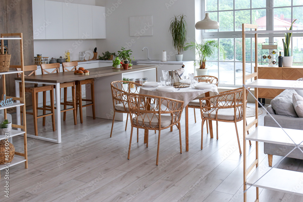 Interior of light open space kitchen with served dining table, island and big window