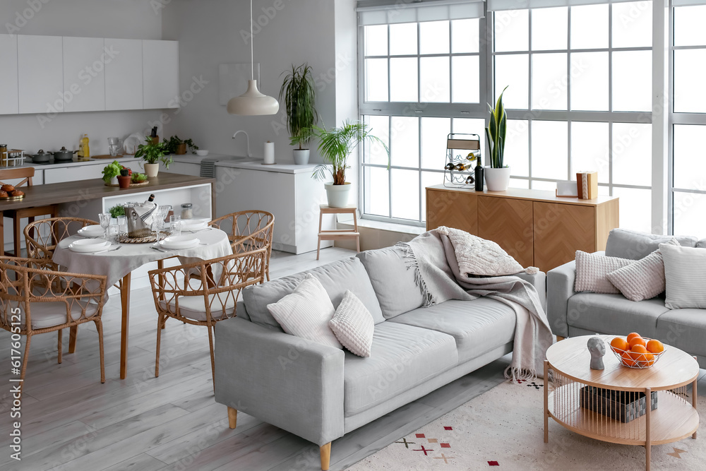 Interior of light open space kitchen with cozy grey sofas and oranges on wooden coffee table