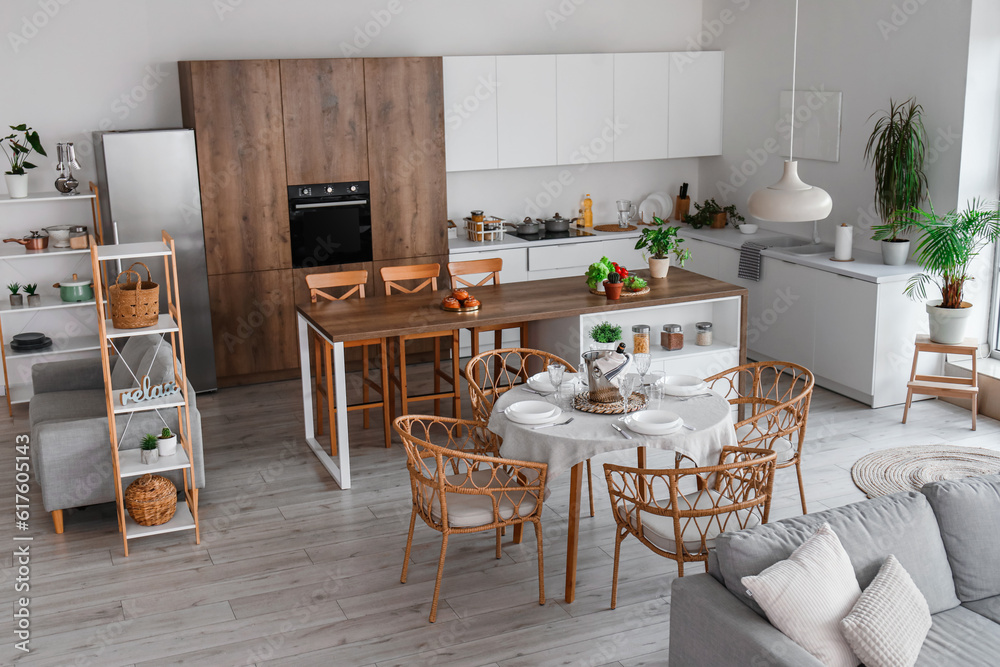 Interior of light open space kitchen with grey sofa, served dining table and island