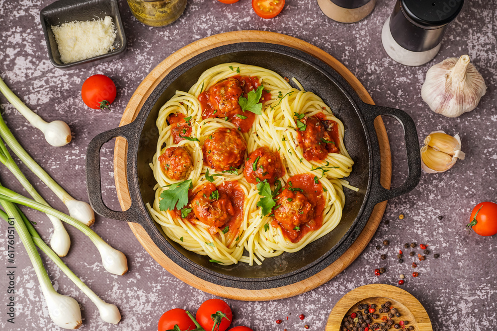 Frying pan of boiled pasta with tomato sauce and meat balls on grey table