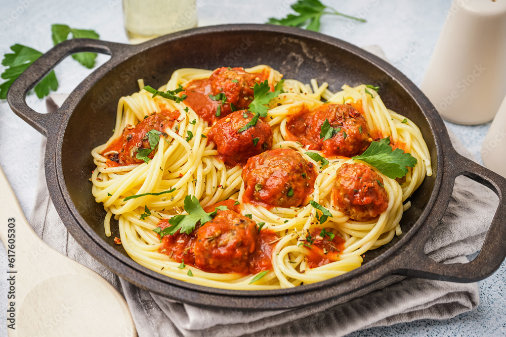 Frying pan of boiled pasta with tomato sauce and meat balls on white table