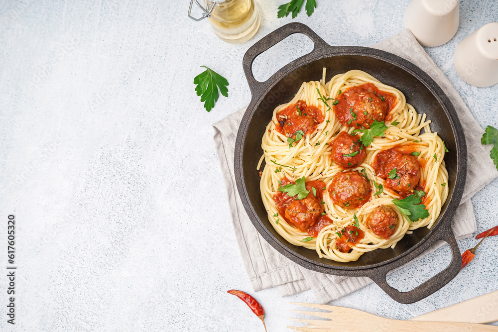 Frying pan of boiled pasta with tomato sauce and meat balls on white table