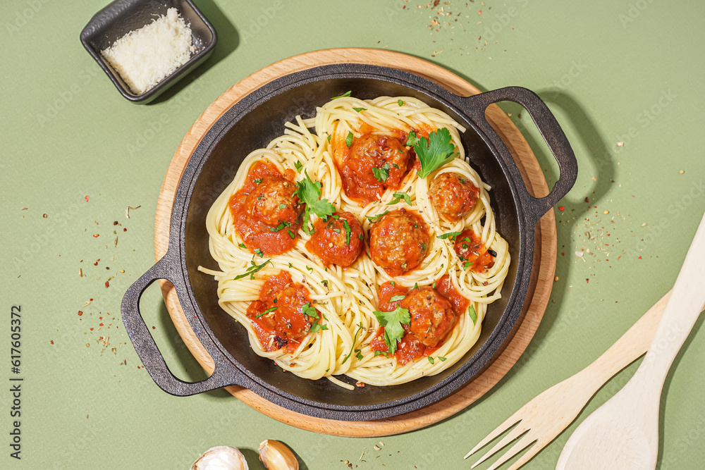 Frying pan of boiled pasta with tomato sauce and meat balls on green background