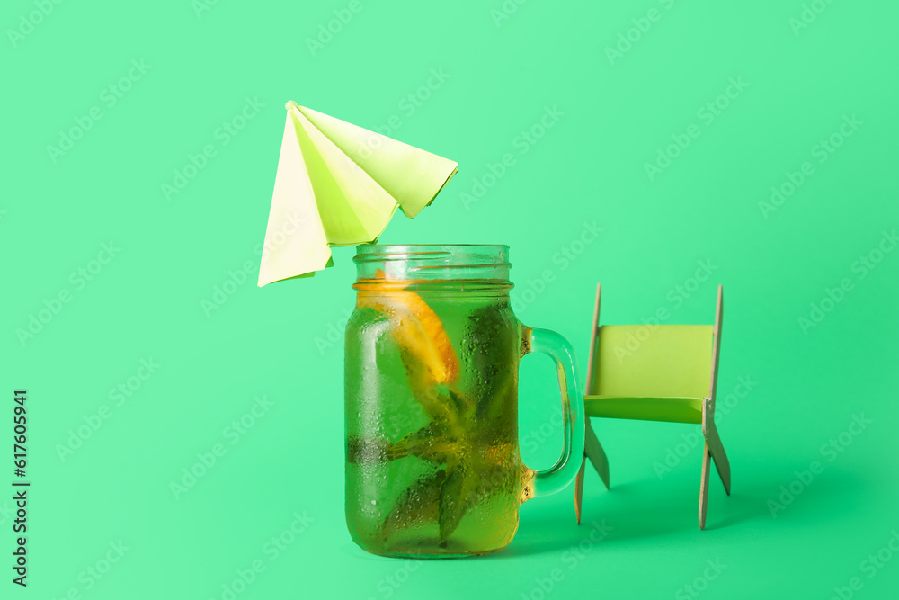 Mason jar of ice tea with lemon and decorative umbrella on green background