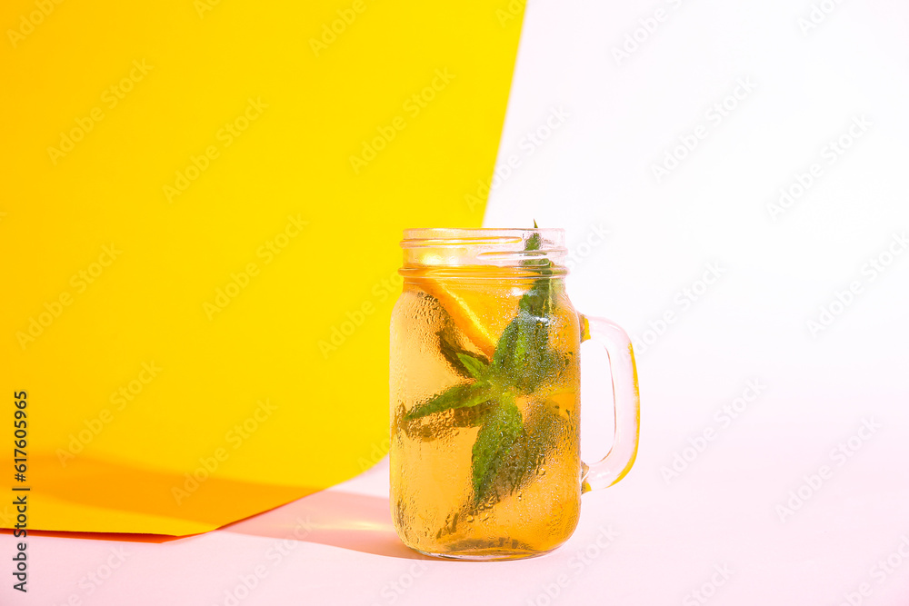 Mason jar of ice tea with orange and mint on colorful background