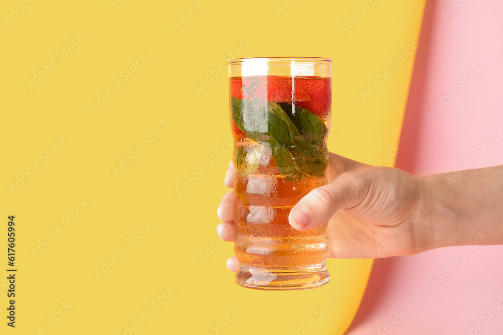 Female hand holding glass of ice tea with strawberry and mint on colorful background