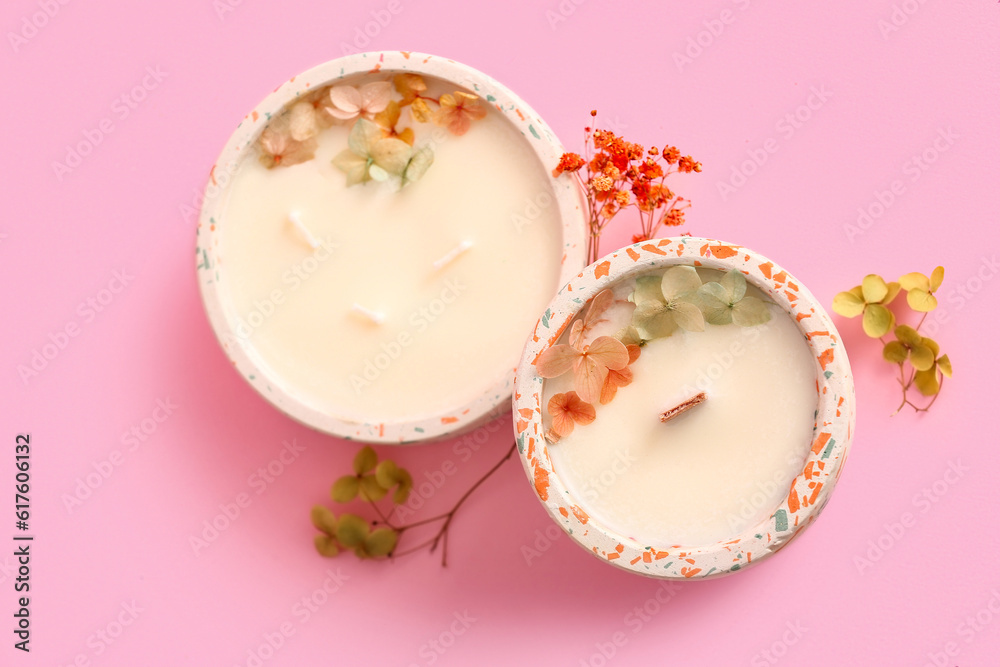 Holders with candles and flowers on pink background