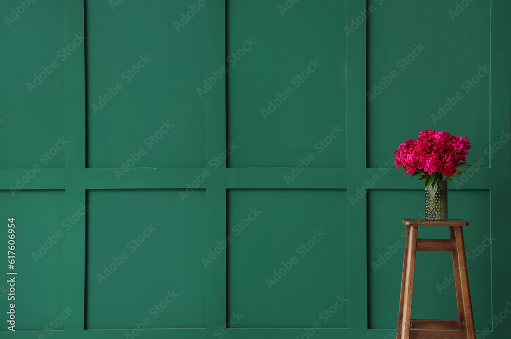 Vase of red peonies on stool near green wall