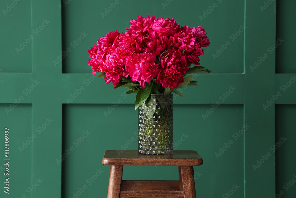 Vase of red peonies on stool near green wall