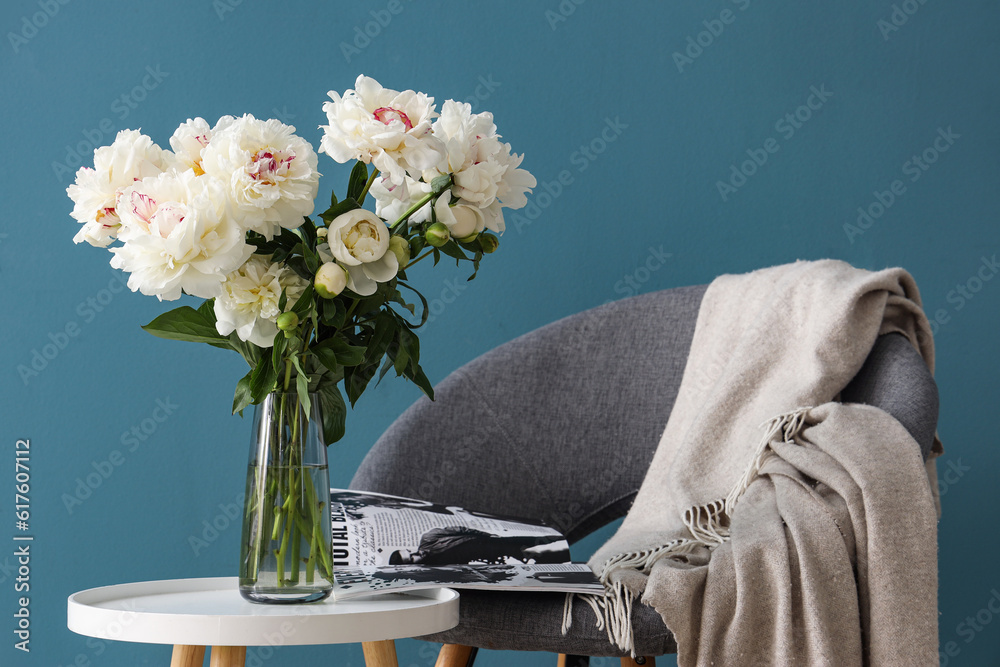 Vase of white peonies with coffee table, chair and magazine near blue wall