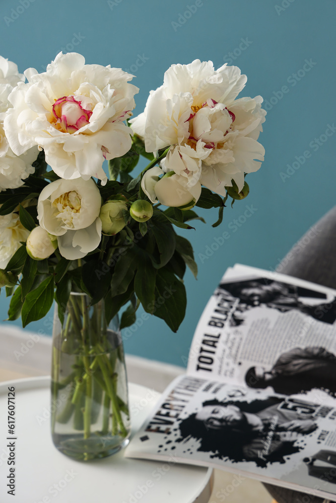 Vase of white peonies with coffee table and magazine near blue wall