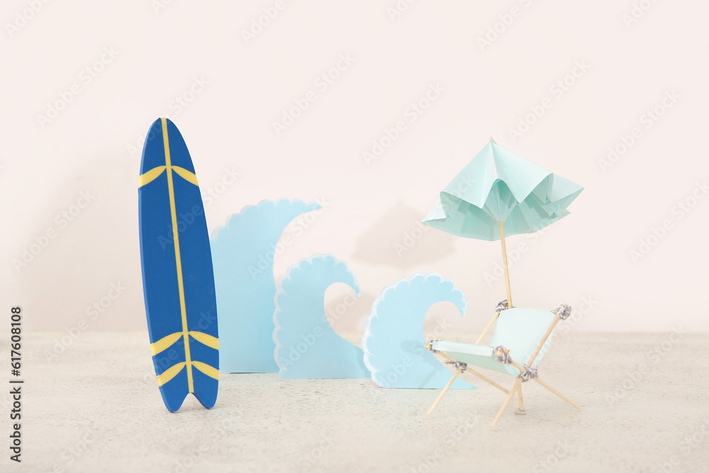 Creative composition with mini surfboard, miniature deckchair and paper waves on white table