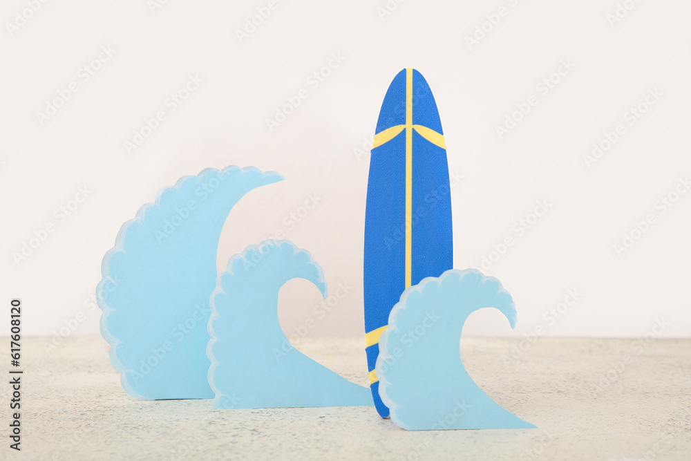 Creative composition with mini surfboard and paper waves on white table