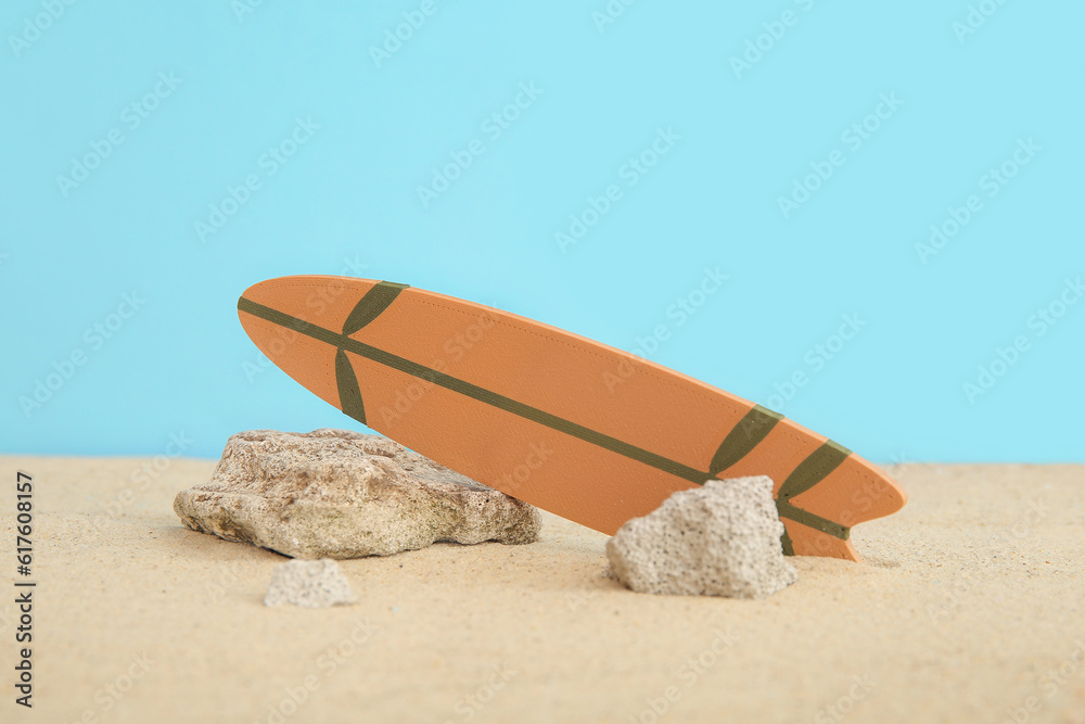 Mini surfboard with stones on sand against blue background