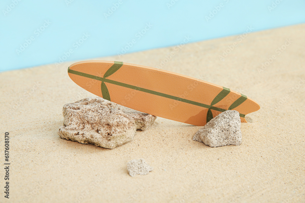 Mini surfboard with stones on sand against blue background