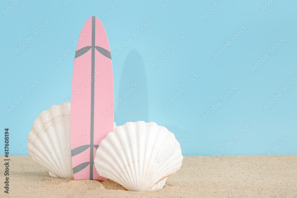 Mini surfboard with seashells on sand against blue background