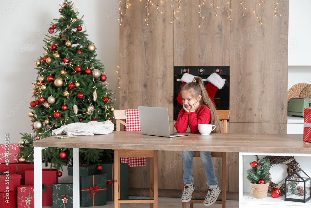 Cute little girl watching cartoons in kitchen on Christmas eve