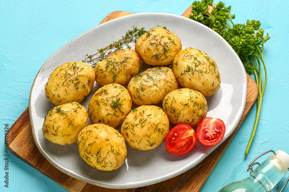 Plate of boiled baby potatoes with dill and tomatoes on blue background