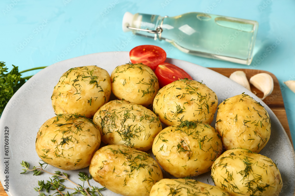 Plate of boiled baby potatoes with dill and tomatoes on blue background