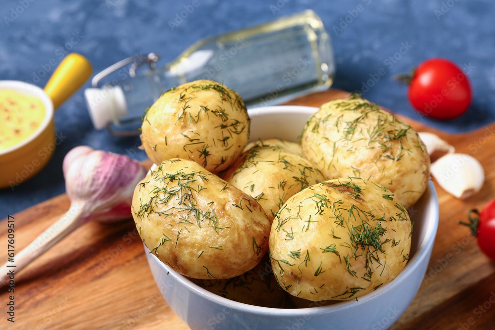 Bowl of boiled baby potatoes with dill and tomatoes on blue background