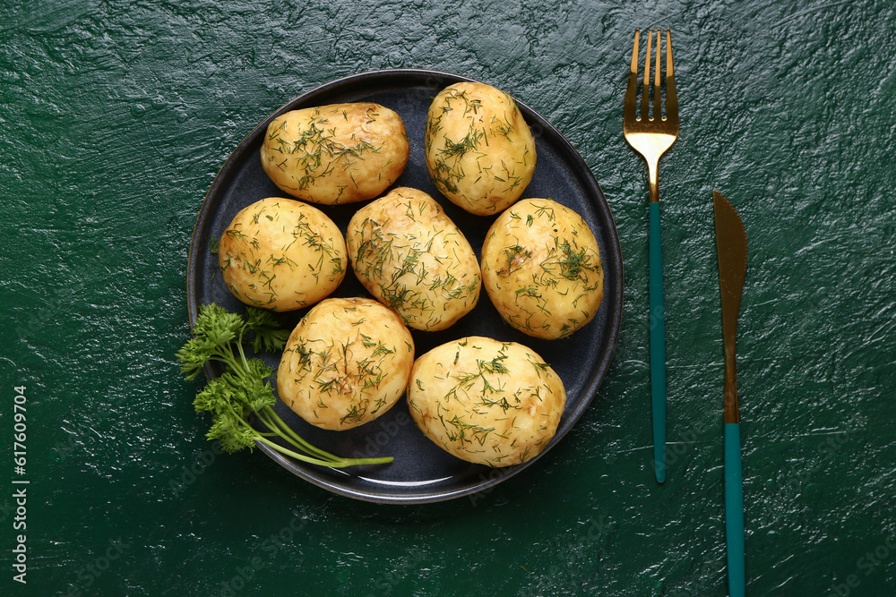 Plate of boiled baby potatoes with dill and parsley on green background