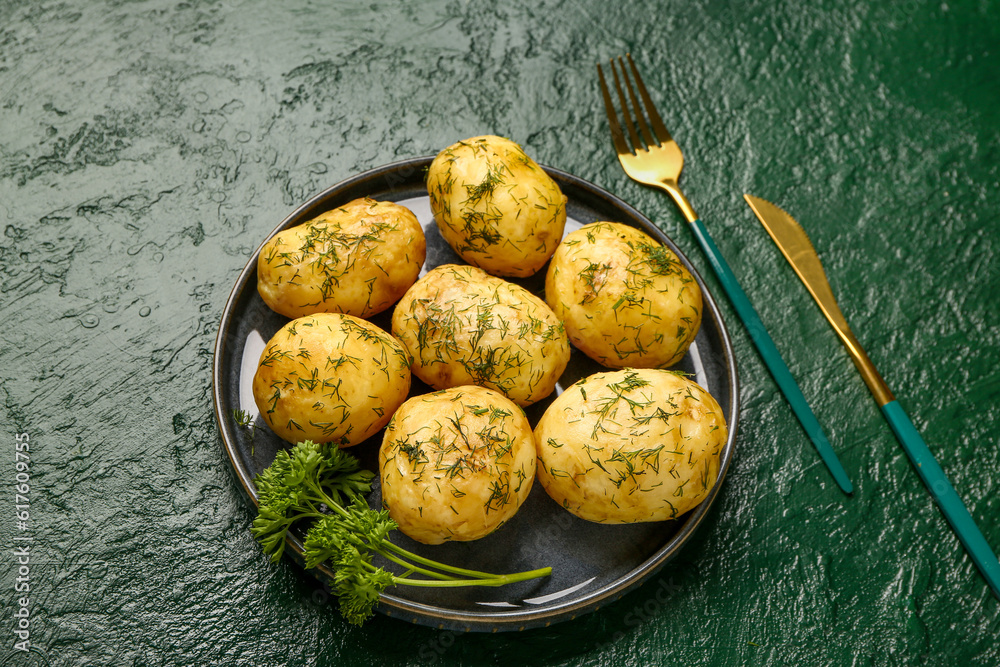 Plate of boiled baby potatoes with dill and parsley on green background