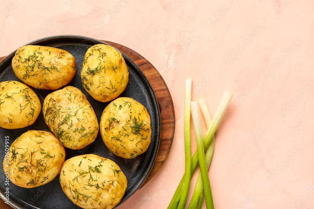 Plate of boiled baby potatoes with dill and green onion on pink background