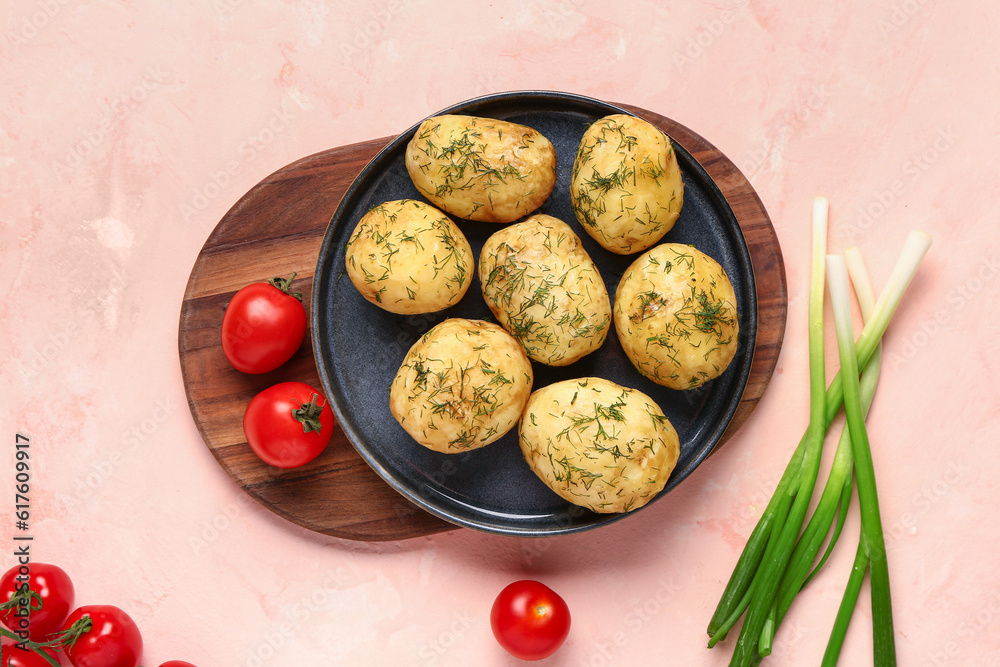 Plate of boiled baby potatoes with dill and green onion on pink background