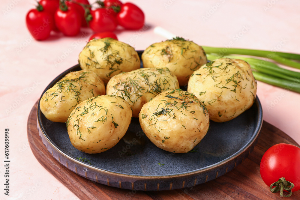 Plate of boiled baby potatoes with dill and green onion on pink background