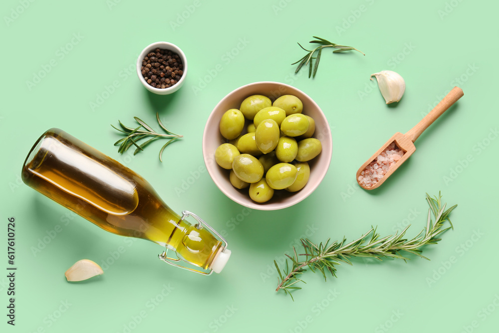 Bowl with ripe olives and bottle of oil on green background