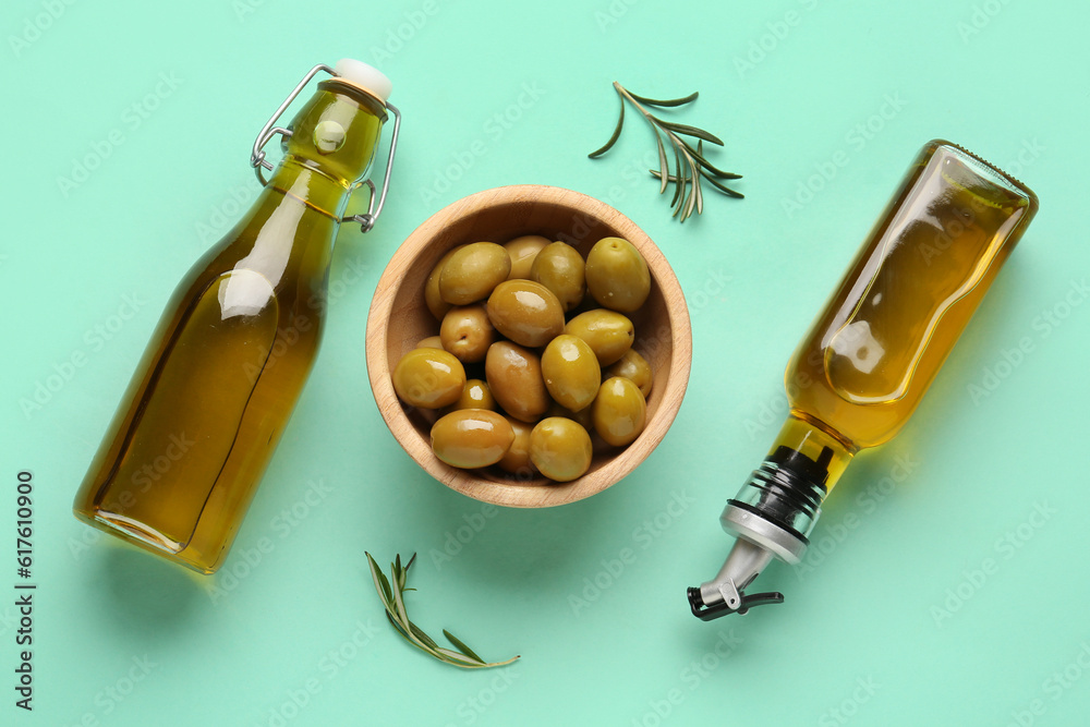 Bowl with ripe olives and bottles of oil on turquoise background