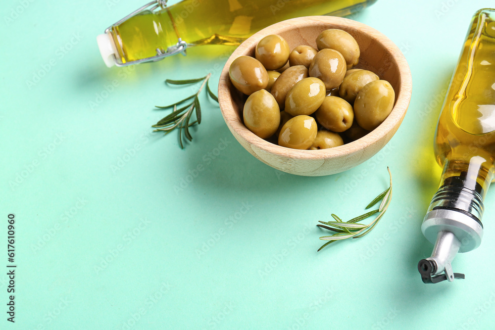 Bowl with ripe olives and bottles of oil on turquoise background