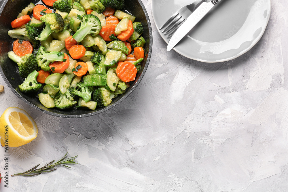 Frying pan with tasty vegetables on grey background