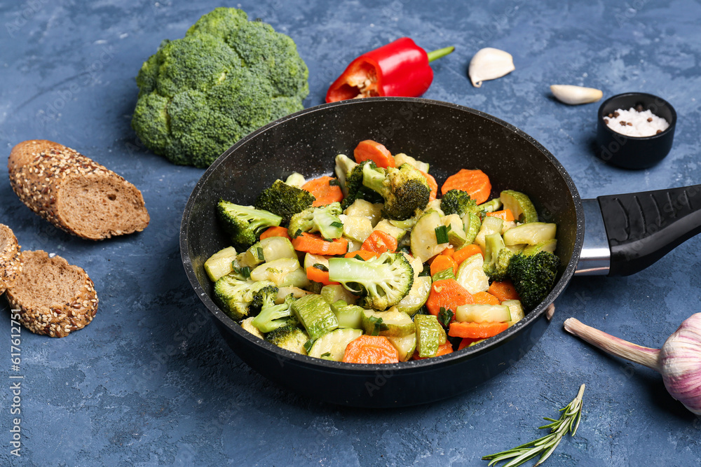 Frying pan with tasty vegetables on blue background