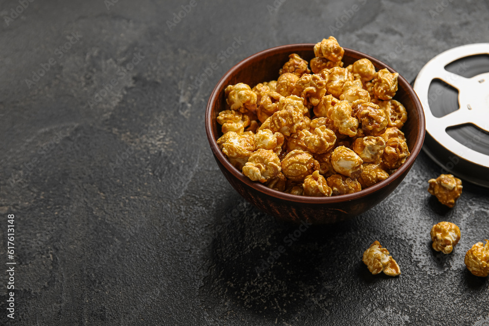 Bowl with tasty popcorn and film reel on black background